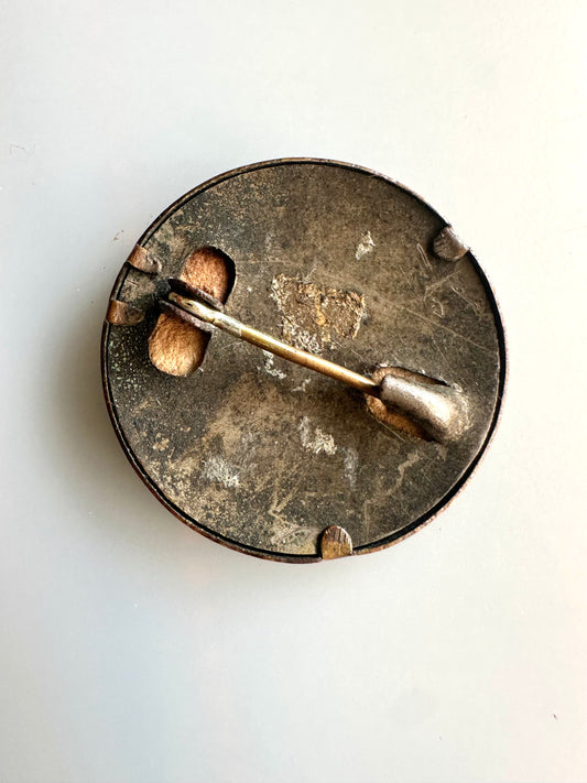 Metallic brooch with a central pin on a white background