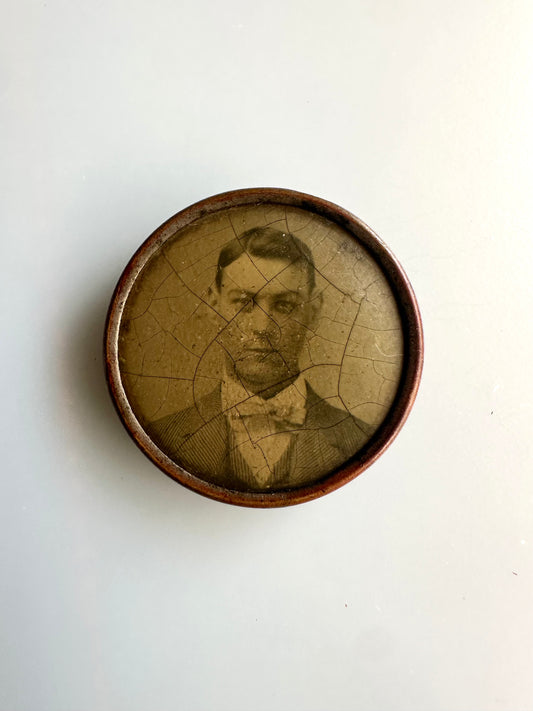 Antique round photograph pin of a handsome man with a bow tie on a white background. 