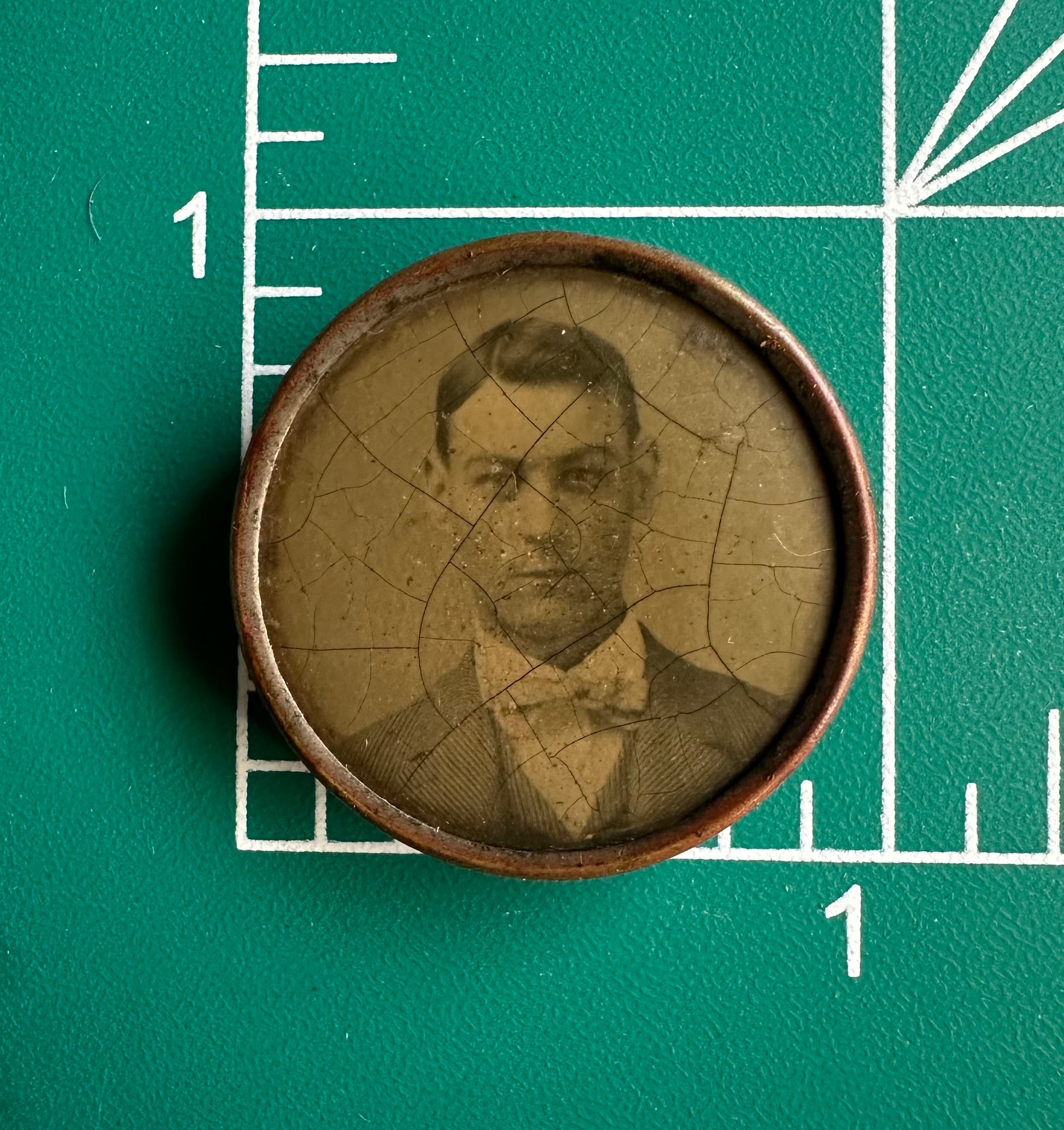 Vintage photograph of a man in a bow tie on a green background with measurement markings.